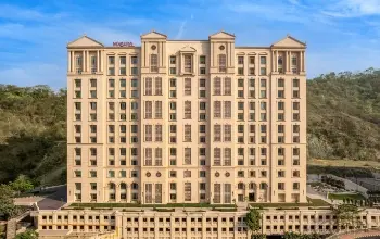 Grand neoclassical-style high-rise building set against a lush green hillside.