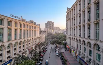 A street view of neoclassical-style commercial buildings with arched windows, lined with palm trees and shops at sunset.