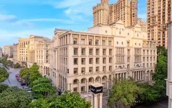 Neoclassical-style commercial building with arched windows and intricate detailing, surrounded by greenery and modern high-rises.