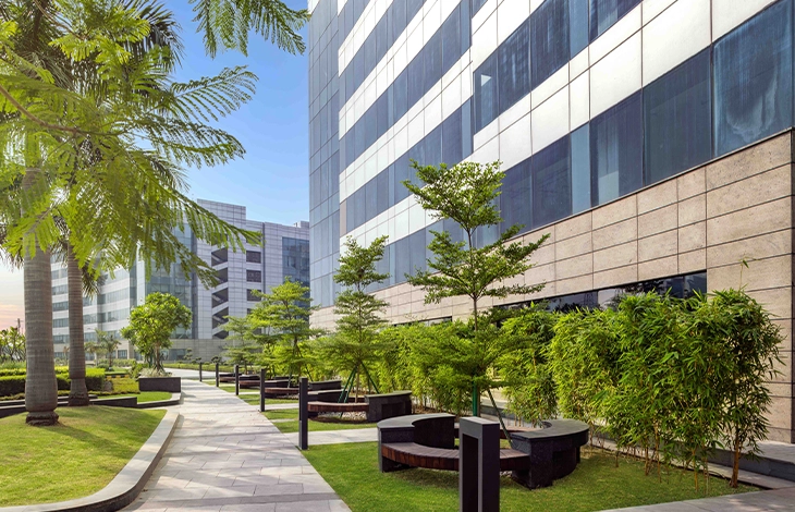 Two individuals admire a colorful mural at Candor TechSpace, Sector 62, Noida. The mural features abstract shapes, clouds, and trees, set against a grassy backdrop