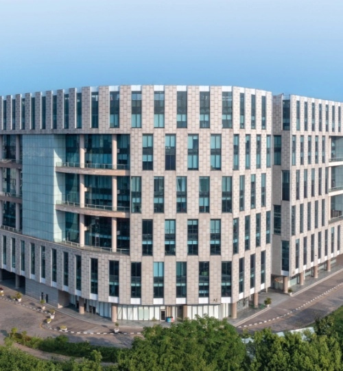 A wide-angle view of Candor TechSpace located in Newtown, Kolkata, showcasing the modern architecture of the building. The image captures the sleek design with expansive glass windows and green surroundings.