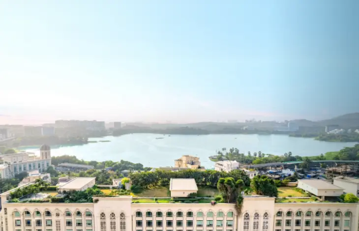 A wide panoramic view of Delphi, located in Downtown Powai, Mumbai, with a beautiful scenic view of the lake in the foreground and the city skyline in the background, under a clear sky.