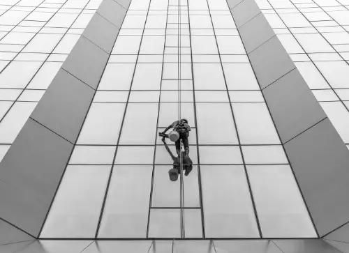 Worker cleaning the glass windows of a tall building, suspended on a rope, showcasing high-altitude maintenance work.