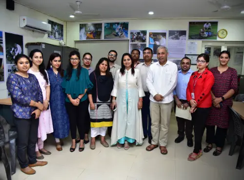 A group of people, including both men and women, posing for a photo in an office setting, with photos of community work displayed on the walls