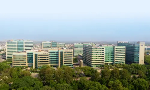 A panoramic aerial view of a modern office complex with multiple glass buildings surrounded by lush greenery, showcasing a thriving business hub
