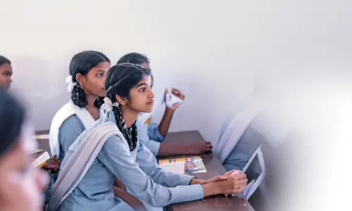 A group of schoolgirls sitting attentively in class, with their hands folded and listening intently.