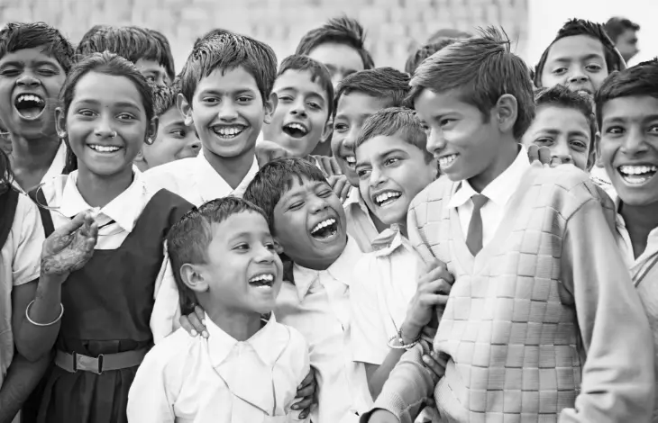 A group of children smiling and laughing together in a joyful moment, captured in black and white.