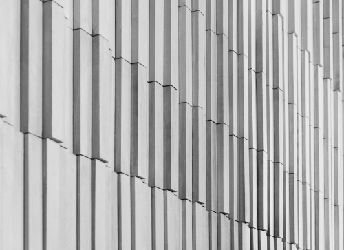 Close-up view of a modern building's exterior featuring a repetitive geometric pattern of vertical lines and sections in a monochrome color scheme, emphasizing the architectural design.