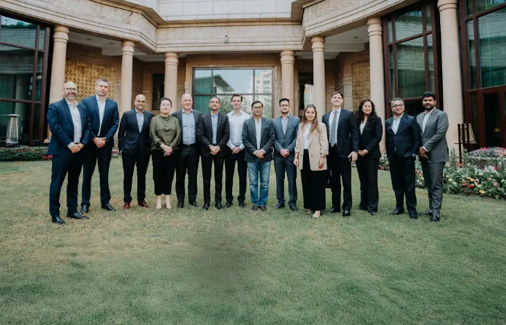 A group of professionals in business attire posing for a photo in front of a classical-style building with columns and glass windows.