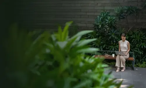 A woman working on a laptop while sitting on a bench in a green outdoor space at Candor TechSpace, Sector 48, Gurugram.