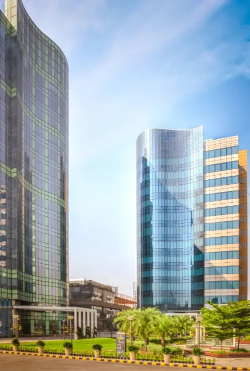 A view of the modern, glass-paneled buildings at Candor TechSpace, Sector 62, Noida, with clear skies and greenery in the foreground.