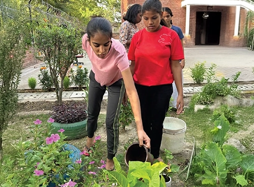 Two young women watering plants in a garden as part of a community or environmental activity